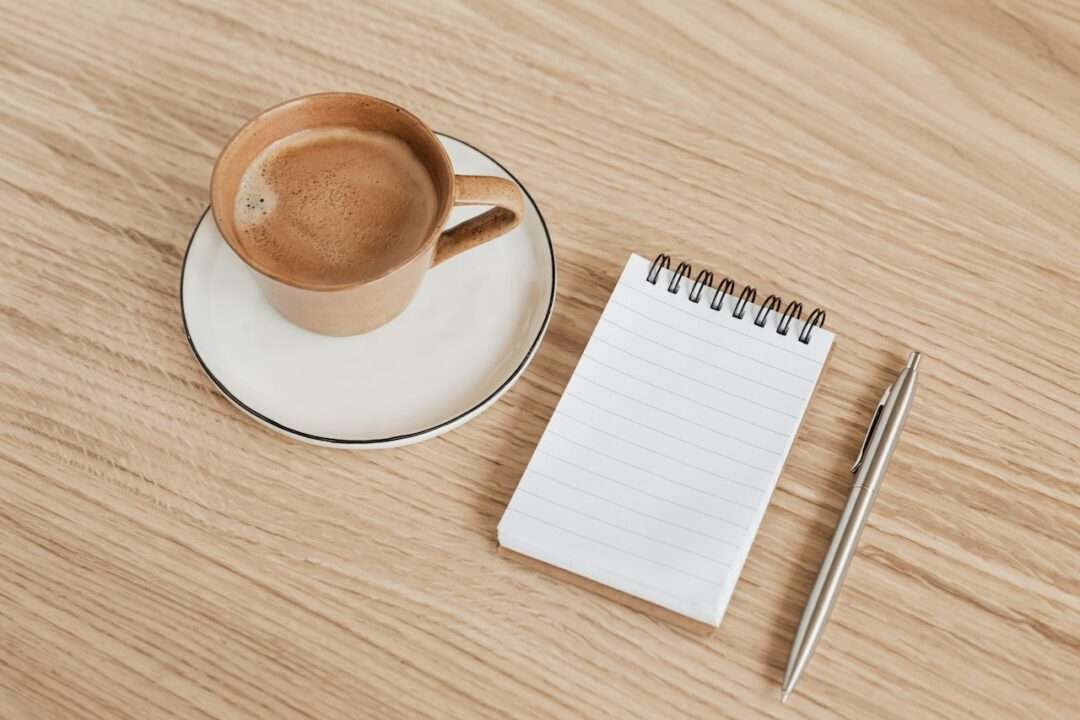 Open notebook with a handwritten evening checklist beside a warm candle and cup of tea on a desk